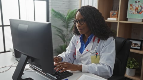 Young Black woman doctor at her desktop computer looking at the screen in disbelief