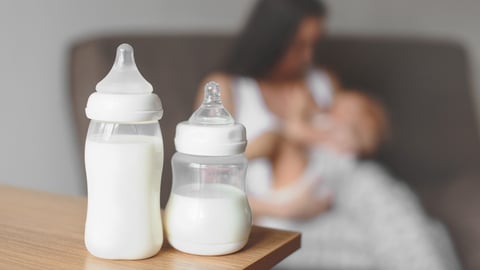 Bottles with breast milk on the background of mother holding in her hands and breastfeeding baby. Maternity and baby care.; Shutterstock ID 1032775489