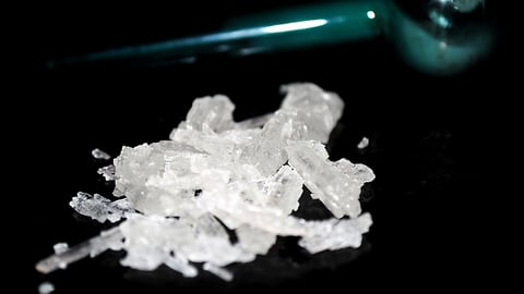 Small pile of methamphetamine crystals with blue glass meth pipe in background.; Shutterstock ID 1314852365