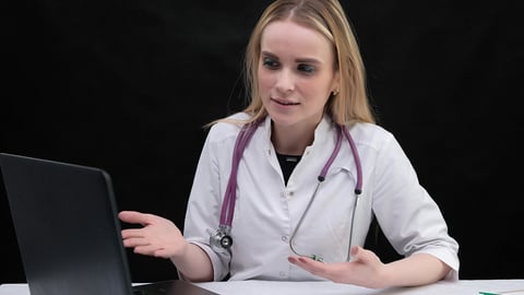 Studio portrait concept of a beautiful fashionable blonde girl a doctor and talking in a business dress on black background sitting with a laptop. She is right in front of the camera, smiling.; Shutterstock ID 1366520270