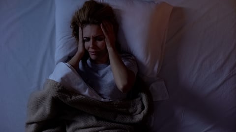 Woman having terrible headache lying in bed at night, strong migraine, top-view; Shutterstock ID 1486449422
