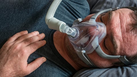 A man in an oxygen mask for CPAP therapy in bed; Shutterstock ID 1675350667