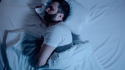 A lonely bearded dark-haired man sleeps soundly on his stomach at night on the bed. General plan from above, orthopedic pillow, bedroom, self-isolation. One; Shutterstock ID 1691821795
