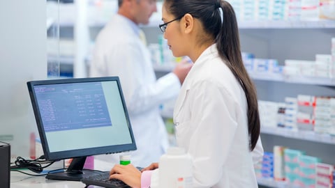 Medium shot of a female pharmacist working on a computer at a pharmacy counter.; Shutterstock ID 1866123349