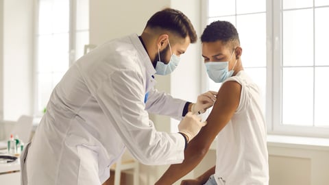 Doctor in medical face mask giving injection to patient during vaccination campaign at the clinic. Young African-American man getting Covid-19, AIDS or flu antivirus vaccine shot at the hospital; Shutterstock ID 1874064979