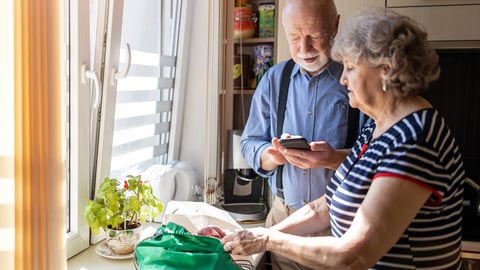 Senior couple using a smartphone while unpacking groceries in the kitchen at home; Shutterstock ID 1962766558