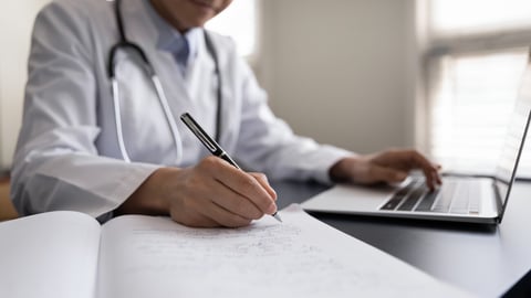 Crop close up Indian woman doctor in white uniform with stethoscope taking notes, using laptop, writing in medical journal, professional therapist practitioner filling documents or patient card; Shutterstock ID 2078659765
