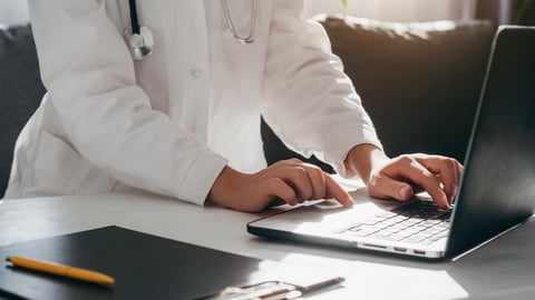 Close up of young woman doctor in white uniform with stethoscope using laptop, writing in medical journal, professional therapist practitioner sitting at table in hospital and typing at computer; Shutterstock ID 2216016273