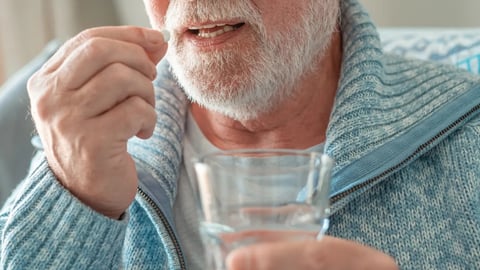Close-up on senior bearded man taking a pill with a glass of water - health care and people concept; Shutterstock ID 2224363825