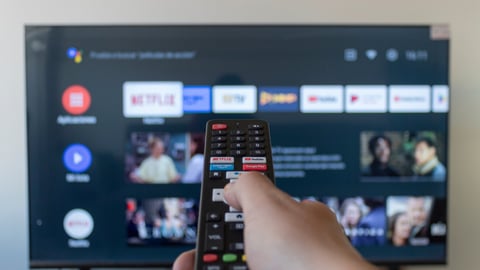 BOGOTA, COLOMBIA - MAY 07 OF 2023 A male hand holding a remote control with android tv interface at background; Shutterstock ID 2300701797