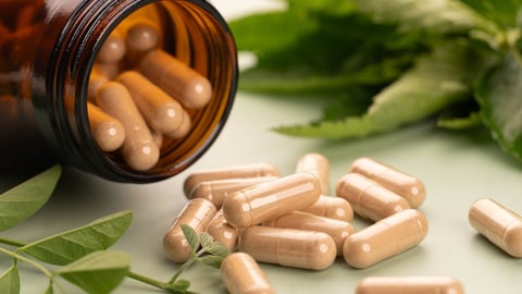 Alternative medicine herbal capsules spilled out of brown glass bottle with fresh organic plant leaf on green background. Natural herbs and homeopathic supplement product for healthy. Close up.; Shutterstock ID 2411344701