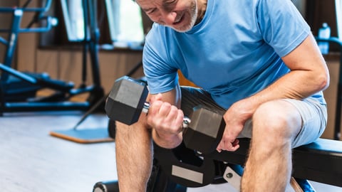 A man is lifting weights in a gym. He is smiling and he is enjoying himself. Concept of positivity and motivation, as the man is working hard to improve his fitness; Shutterstock ID 2474151279