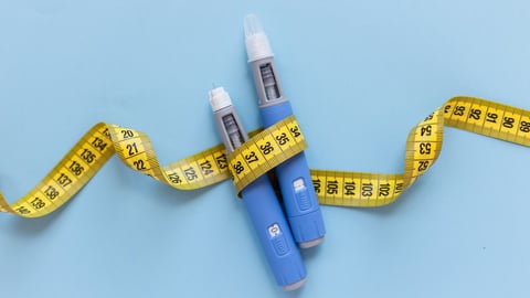 Two injectors dosing pens for subcutaneous injection of antidiabetic medication or anti-obesity medication hovering over a blue background. Yellow measuring tape around the injectors.; Shutterstock ID 2492168829