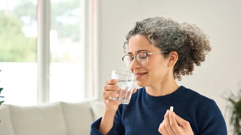 Happy healthy woman of middle age talking pill holding glass of water standing at home. Mature 50 years old lady taking vitamin health care supplement morning daily nutrition treatment concept.; Shutterstock ID 2516642939