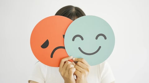 Woman hands holding sad face hiding behind happy face, bipolar and depression, mental health, split personality, mood change concept