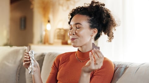Happy, woman and eating chocolate on sofa for morning snack, enjoy candy and sweet tooth for dessert. Smile, girl and eyes closed with cacao sugar for breakfast peace, comfort food and relax at house; Shutterstock ID 2523178463