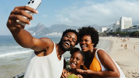 A cheerful Brazilian family enjoys a sunny day at a beach in Rio de Janeiro, capturing the moment with a selfie. The scene showcases joy and togetherness, with the iconic cityscape in the background.; Shutterstock ID 2545766889