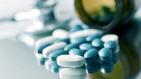 closeup of the desk of a doctors office with a bottle with pills in the foreground and a stethoscope in the background; Shutterstock ID 562215688