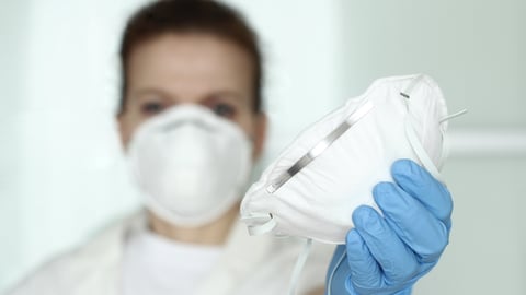 A healthcare worker wears and holds an N95 respirator