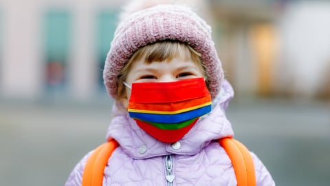 Little girl wearing mask and winter jacket, looking happy