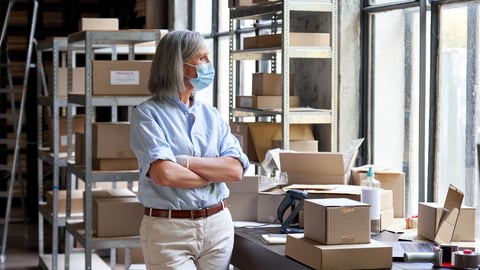 Grey haired woman wearing a mask in a small warehouse