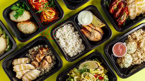 A number of take-out containers filled with healthy meals such as salmon and rice with a dipping sauce.