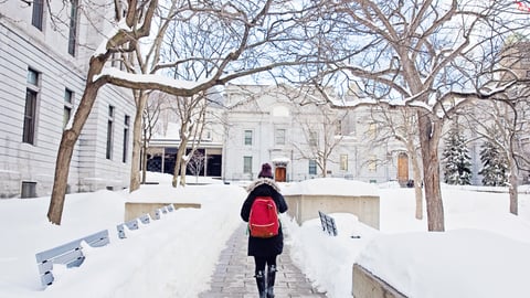A woman wearing a toque and a red backpack walks along a snowy path on McGill campus
