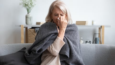 A gray haired women sniffling with a cold on her bed
