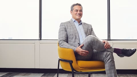 Middle aged white man sitting in a yellow chair wearing a grey suit