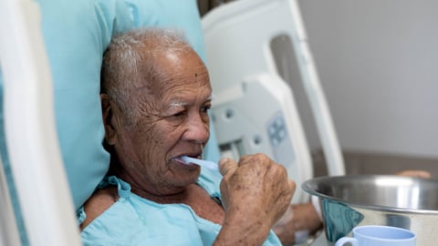 elderly man in hospital bed brushing teeth