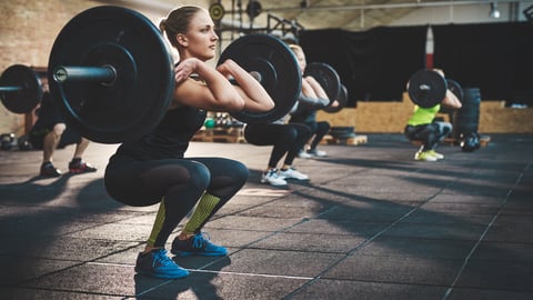 Young white woman squatting to lift a heavy weight at the gym