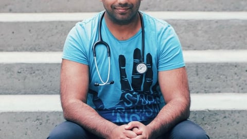 South Asian male physician in blue shirt sitting on steps