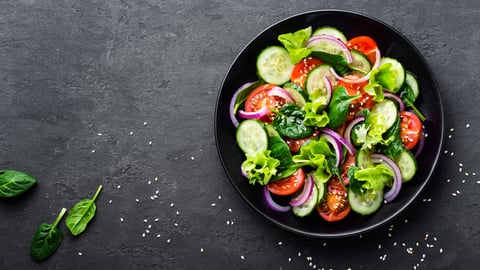 bowl of salad with cucumber, onion, tomato lettuce and sesame seeds