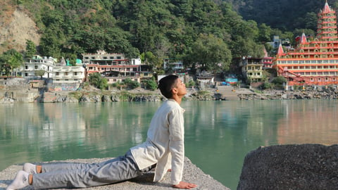 An asian man doing cobra stretch outside ashram