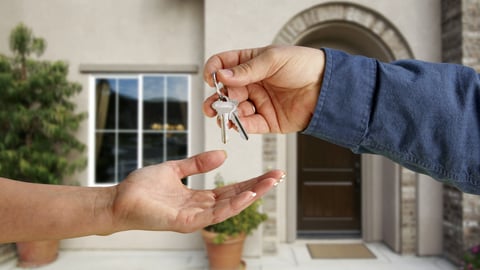 One hand giving another hand keys, with house in background