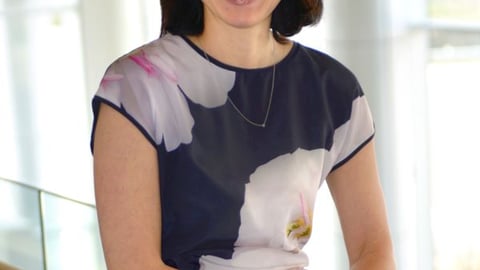 A woman wearing glasses leans on a railing