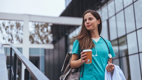 Young female doctor in scrubs carrying coffee outside going or coming from work