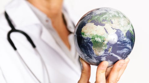 a physician in a white coat holds up a miniature planet Earth