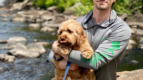 Dr. Tristan Brownrigg sitting by a stream with a dog