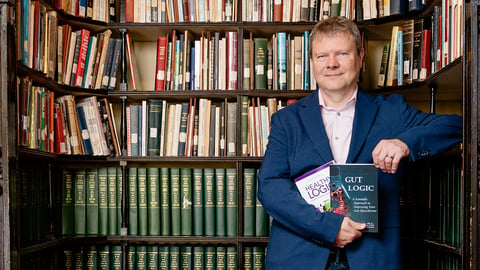 Graham MacKenzie holding his two books in front of a grand bookshelf