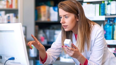 a pharmacist holds a product in her hand as she checks the computer for information