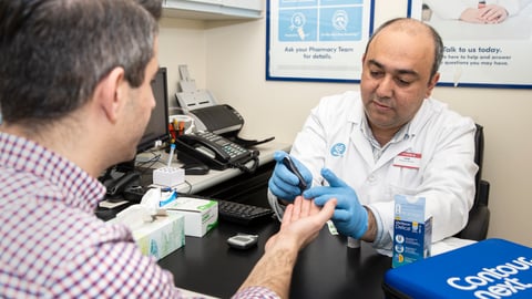 A pharmacist pricks a patient’s finger for a blood glucose test