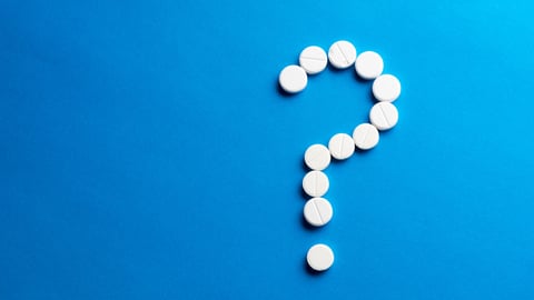 white pills in the shape of a question mark sit on  a blue background