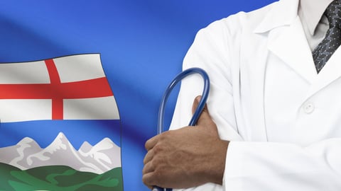 A doctor holds a stethoscope in front of the Alberta flag