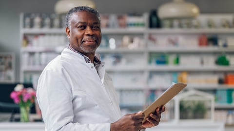 Older Black male pharmacist smiling holding a clipboard