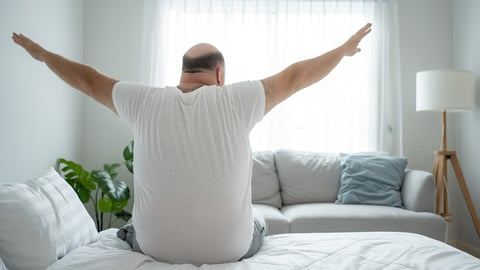 Larger middle-aged white man stretching in bed before starting his day