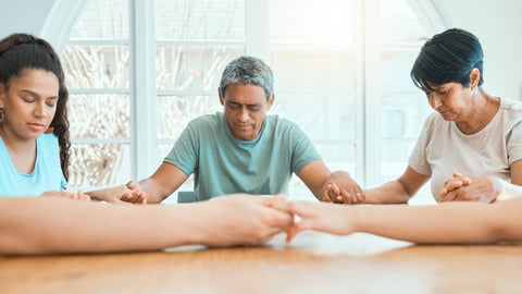 A family with bowed heads holding hands in prayer