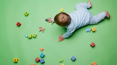 Baby crawling on green floor, surrounded by letter toys