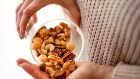 Closeup of hands, woman's, pouring nuts out of glass jar into her hands