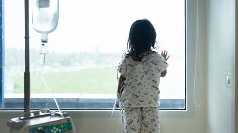 Little girl in pyjamas in hospital, intranvenous in arm looking out window